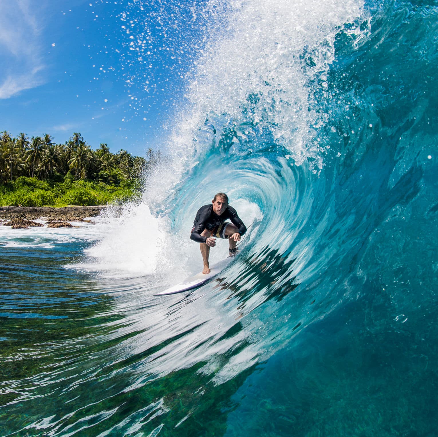 Surfer riding a clear turquoise barrel with palms behind