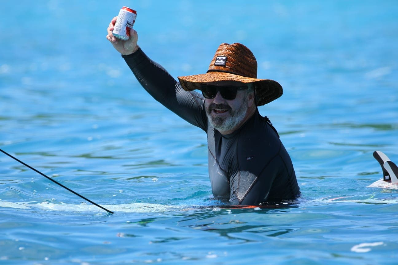 Man in the water holding up a cold beer after a session
