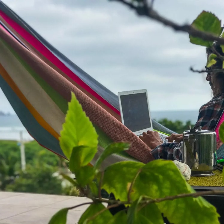 A laptop open in a hammock with the garden behind