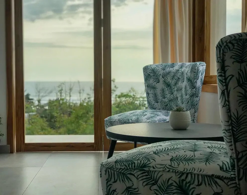 Two patterned armchairs and a table at a window looking out to the sea