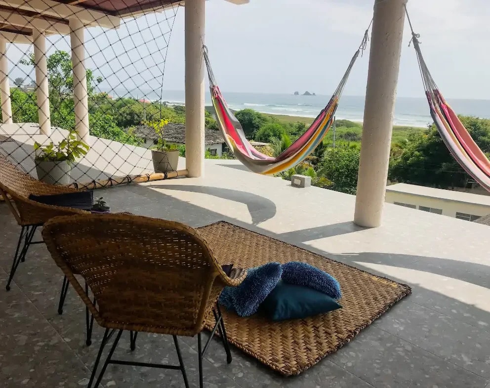 Hammocks and wicker chairs on the terrace, the beach and the rocks beyond