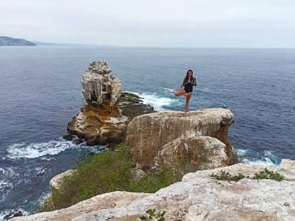 A guest standing in tree pose on the rocks above the sea
