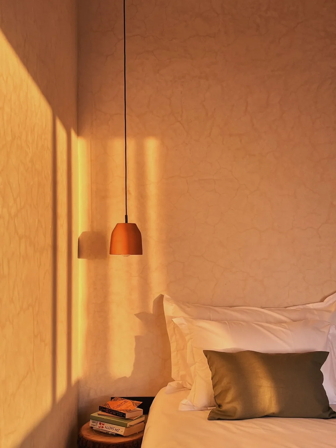 Late light across the wall of a room, with a terracotta pendant over the bed