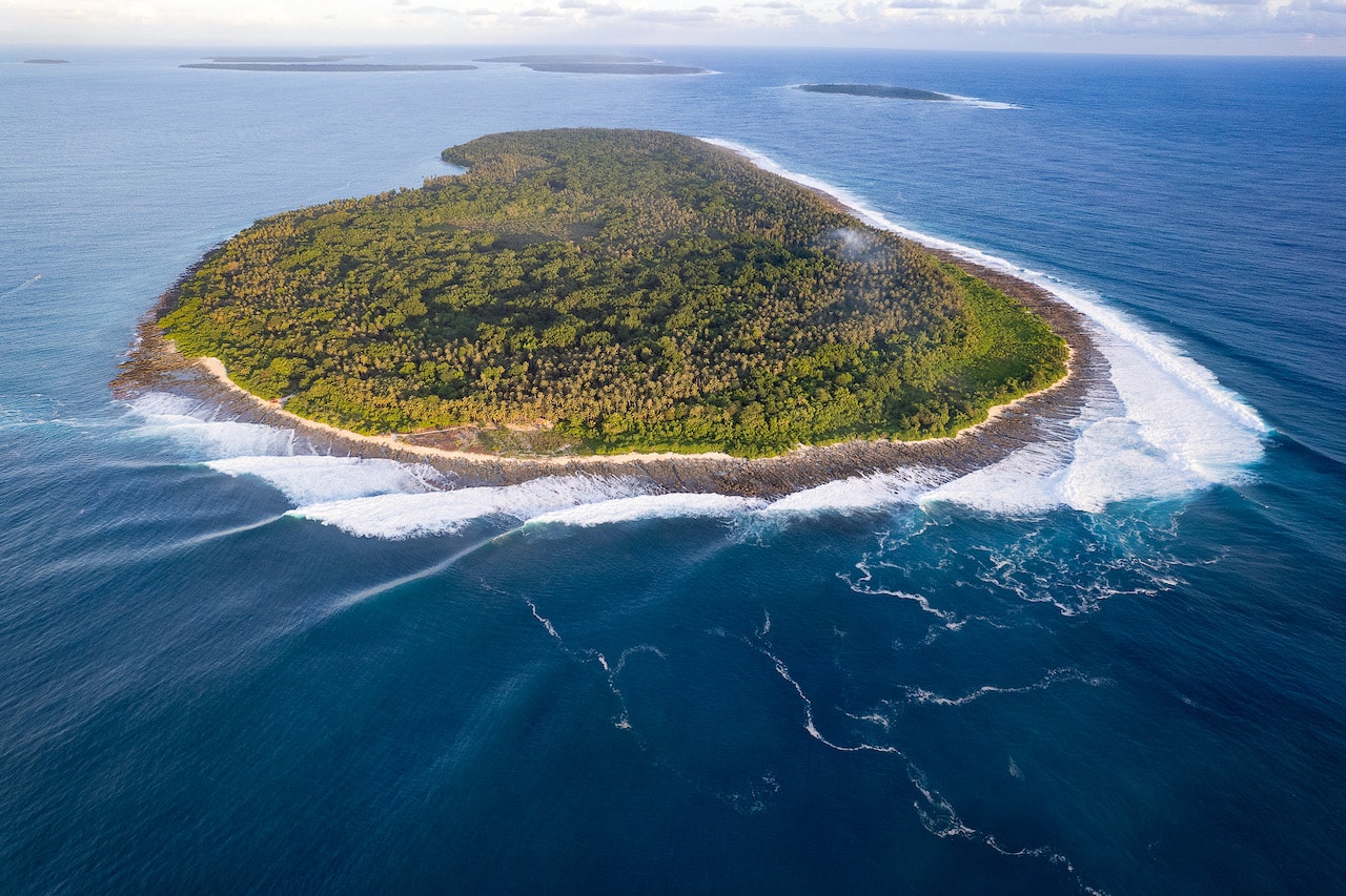 Aerial view of Asu Island ringed by breaking whitewater, with neighboring Hinako islands behind