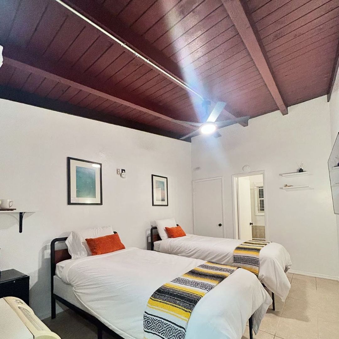 Twin beds under a dark wood beamed ceiling, with Mexican blanket runners