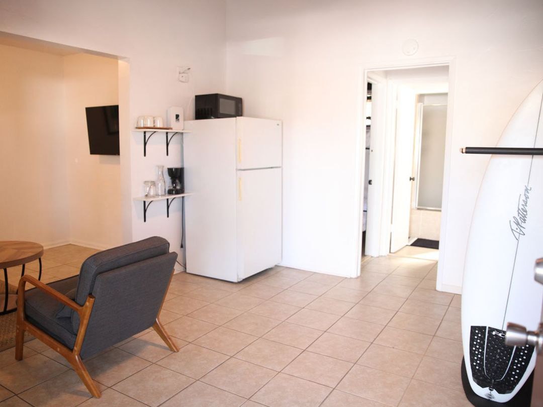 A room with a fridge, microwave, television and a surfboard by the door