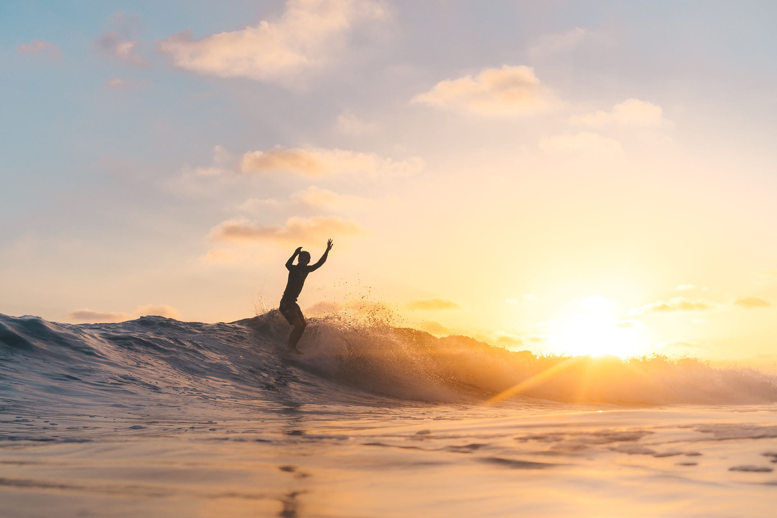 A surfer riding a wave into the sunset off the California coast