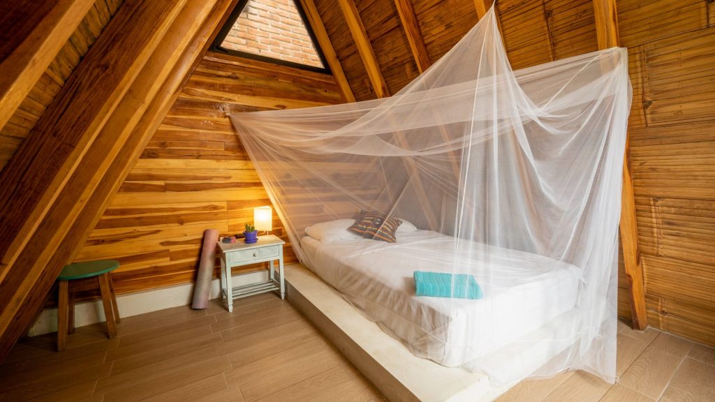 Teak A-frame room with a mosquito net over a platform bed and a yoga mat against the wall
