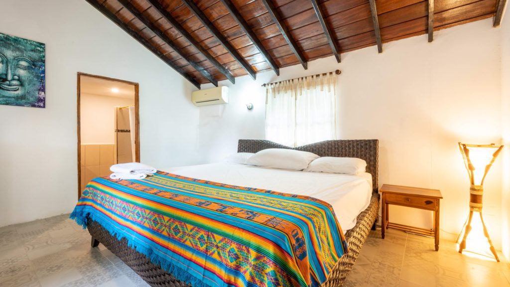 Room with white walls, a beamed wooden ceiling, air conditioning and an Andean blanket on the bed