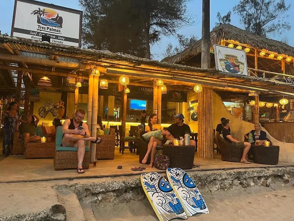 Tres Palmas sign and beachfront bar at dusk with guests seated
